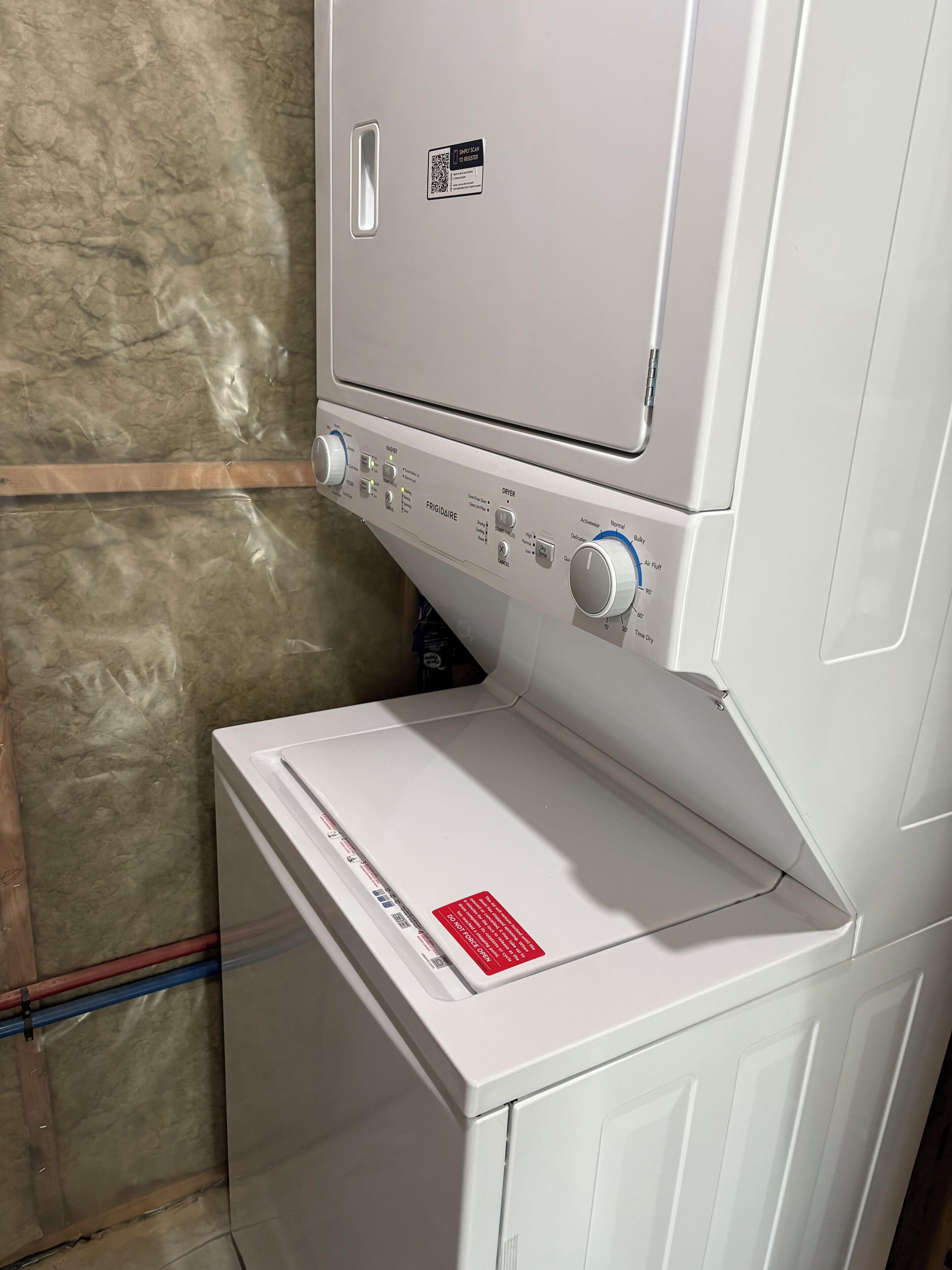 Une machine à laver blanche, dotée d’un panneau de commande, d’un code QR et d’une étiquette de sécurité rouge.