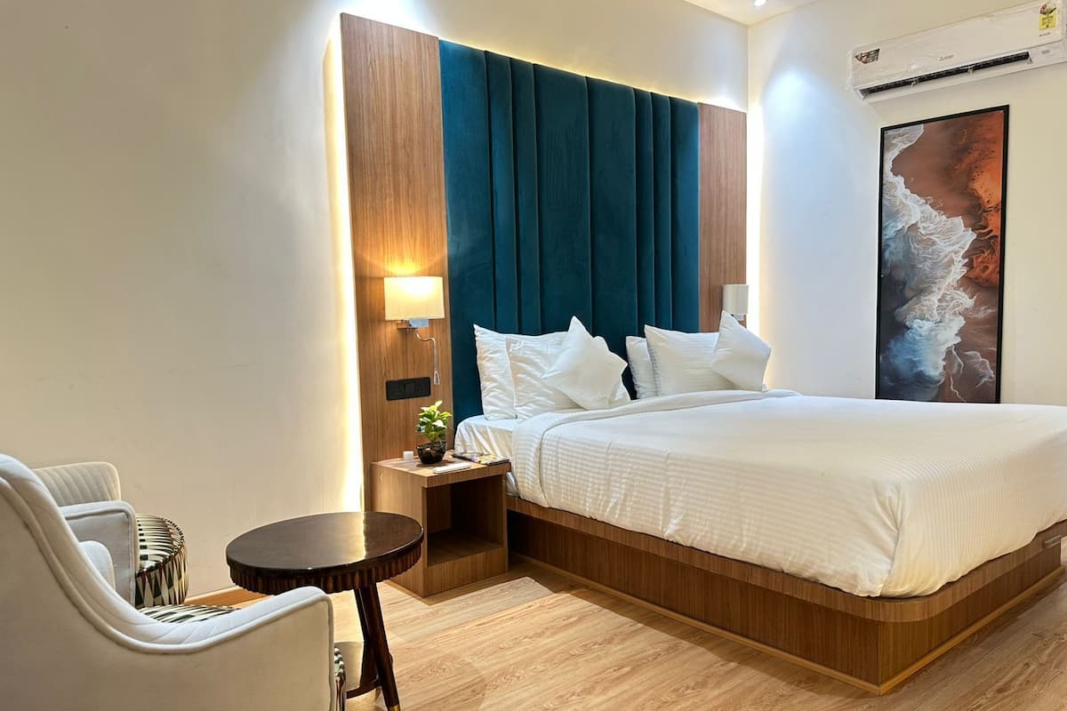 A hotel room with a large bed, a bedside table with a lamp, a chair, and a small table.