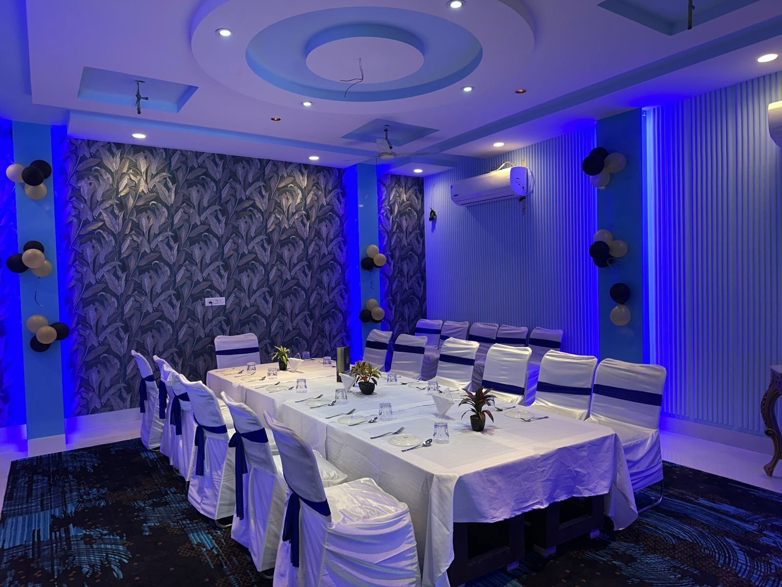 A conference room with a long table, white tablecloths, and chairs with blue sashes.