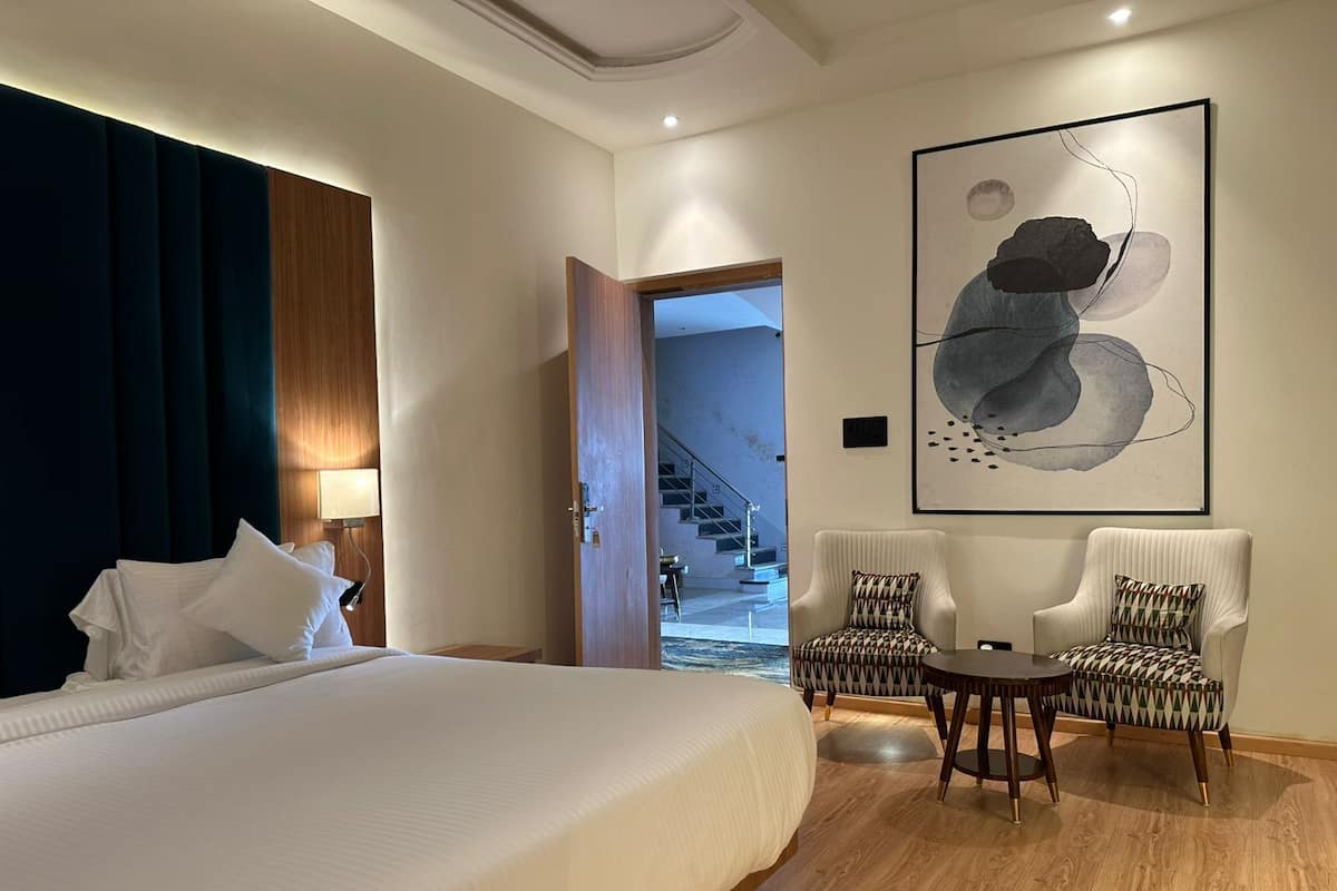 A hotel room with a large bed, two armchairs, a round table, and a modern abstract painting on the wall.