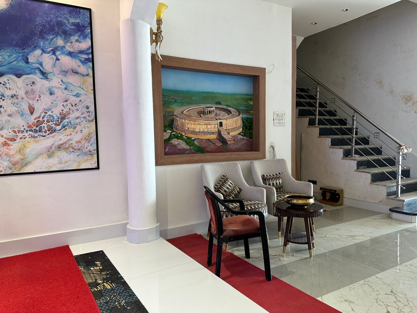 A spacious living area with a large abstract painting, a framed landscape painting, a staircase, and modern furniture.