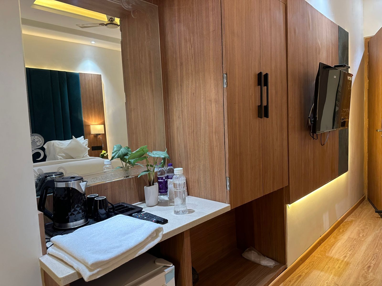 Una habitación de hotel con un armario de madera, una mesita de noche con hervidor, control remoto y espejo.