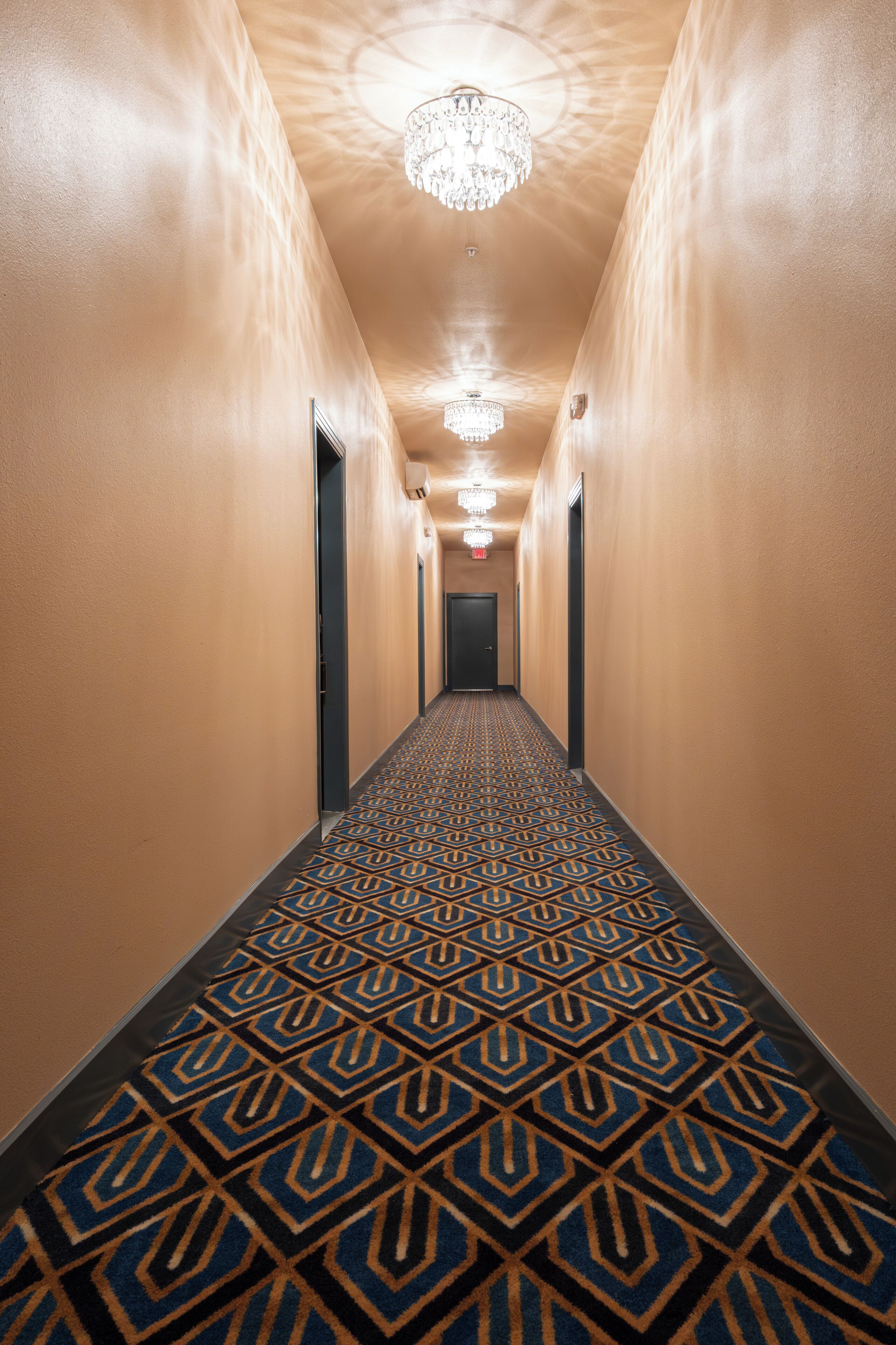 Un pasillo con alfombra estampada, un candelabro y puertas a ambos lados.