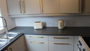 Keittiössä on valkoiset kaapit, leivänpaahdin ja vedenkeitin, jotka ovat sijoitettu työtasolle.