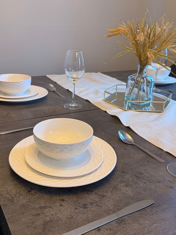 A table set with white bowls, a wine glass, and a vase with dried plants.