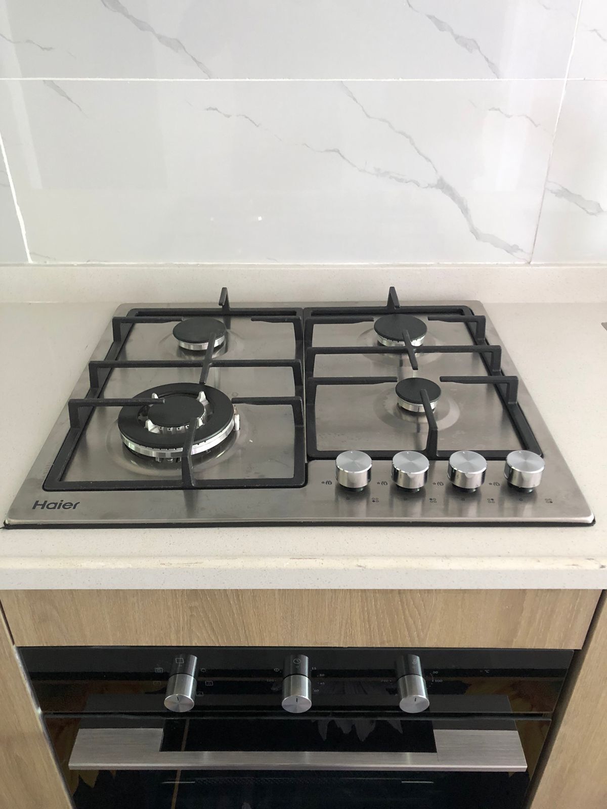 A Haier gas stove with four burners and a control panel, located in a kitchen with a marble backsplash.