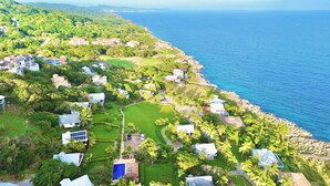 Vue aérienne d’un quartier résidentiel situé sur la côte, avec des maisons, une piscine et une vue sur l’océan.
