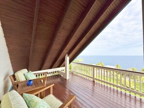 A covered outdoor area with wooden flooring, a white railing, and a view of the ocean.