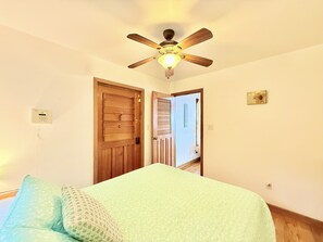 Une chambre à coucher avec un lit, un ventilateur de plafond, une porte en bois et un interrupteur fixé au mur.
