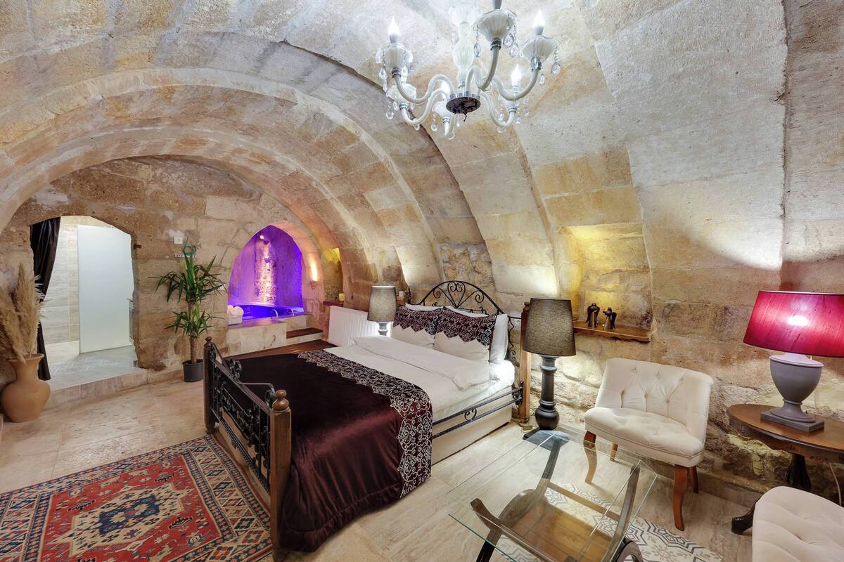A spacious bedroom with a large bed, a sitting area with a chair, and a stone archway leading to another room.