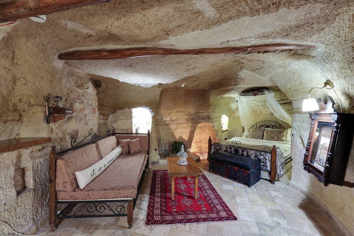 A rustic room with a stone ceiling, a wooden bed, a sofa, and a small table.