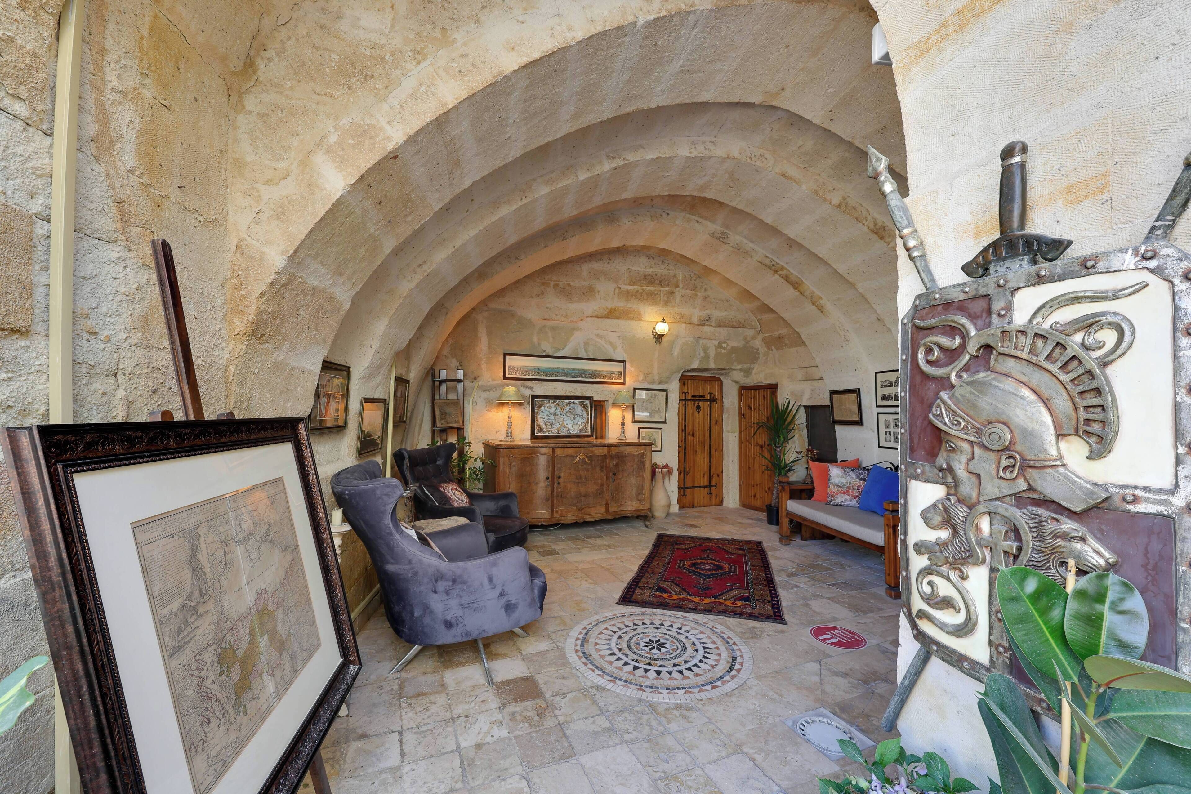 An interior with an arched stone ceiling, a framed map on the left, a sofa, and a decorative shield on the right.