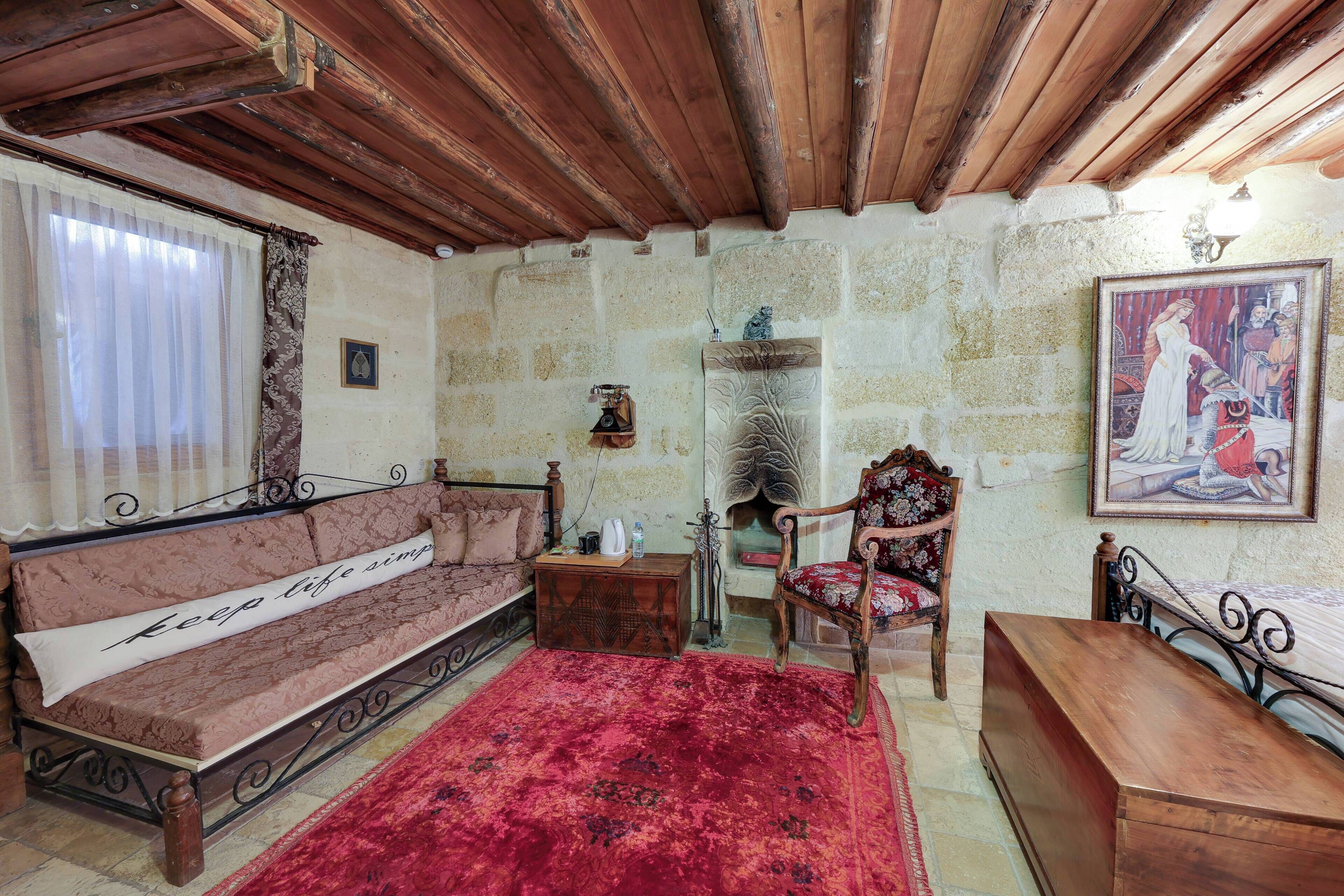 A cozy room with a wooden ceiling, a red carpet, a bench, a sofa, a chair, and a fireplace.