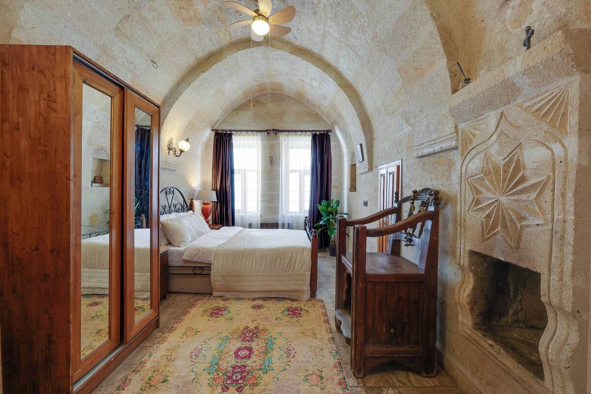 A bedroom with a large bed, wooden furniture, a fireplace, and an arched ceiling.