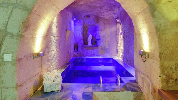 An arched stone bath with a blue-lit interior, a wooden bench, and a basket of towels. - Castle Inn Cave Cappadocia (Nevşehir)