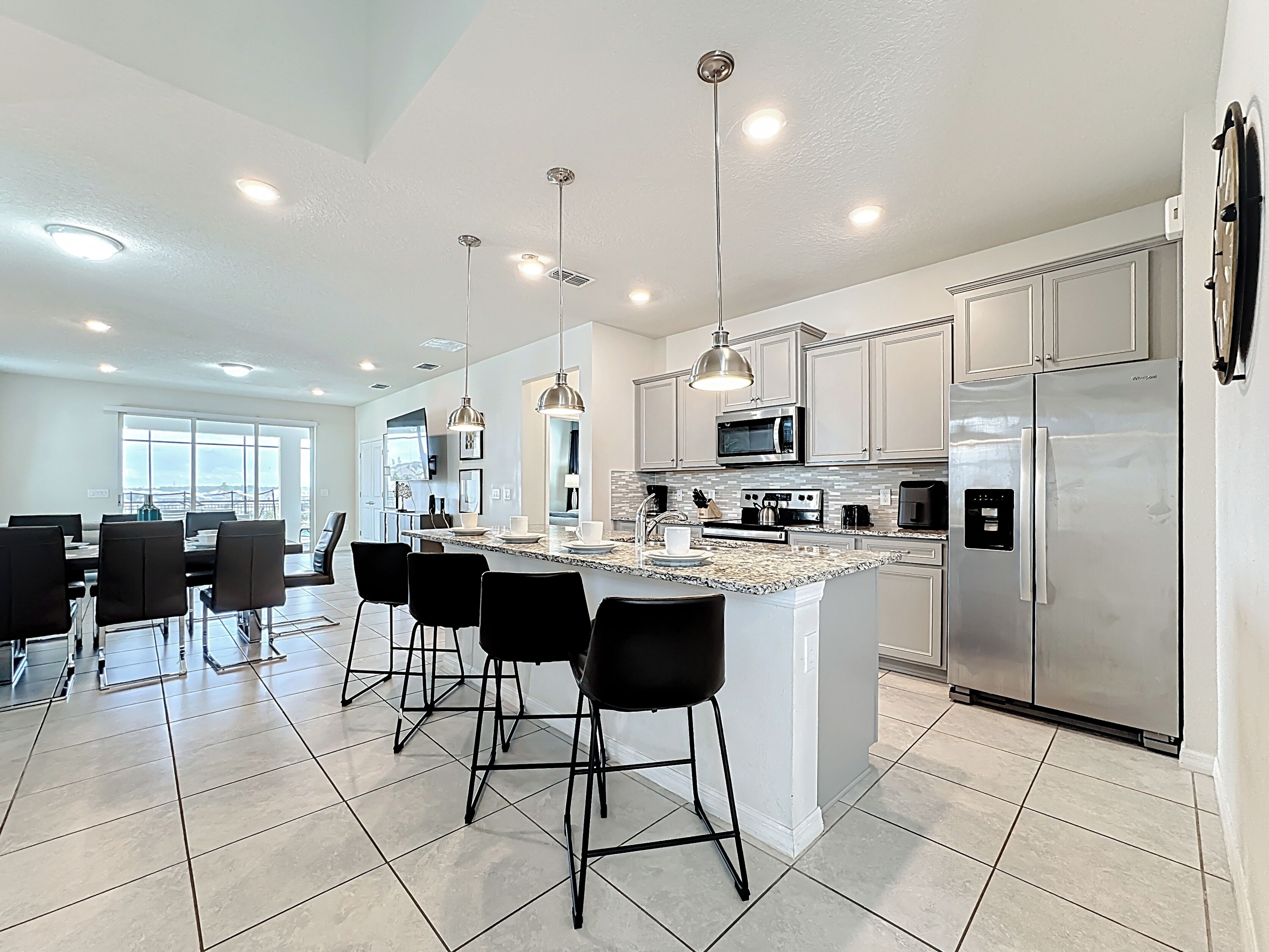 A modern kitchen with a central island, stainless steel appliances, and black bar stools.