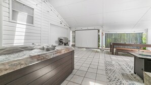 Ein Whirlpool mit einer Holzbank, einem Grill und einer überdachten Terrasse mit Blick auf Grünflächen.