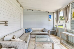 Eine überdachte Veranda mit einem Rattan-Sofa, einem Glastisch und einer Bank.