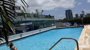 Ein Schwimmbecken mit Glasumrandung, einer Metallleiter und einer gefliesten Terrasse.