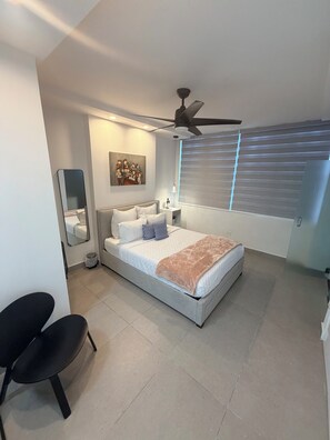 Un dormitorio con cama, ventilador de techo, obras de arte y una ventana con persianas.