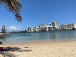 Una playa con un horizonte urbano al fondo, que incluye un hotel llamado "Calle Del Aire".
