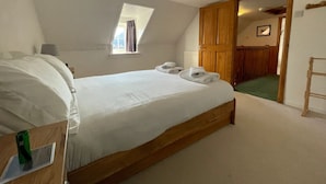 A bedroom with a large bed, a window, a wooden wardrobe, and a green carpeted area. - HAWTHORN DENE, pet friendly, cosy croft cottage with mountain views in Torrin (Torrin)