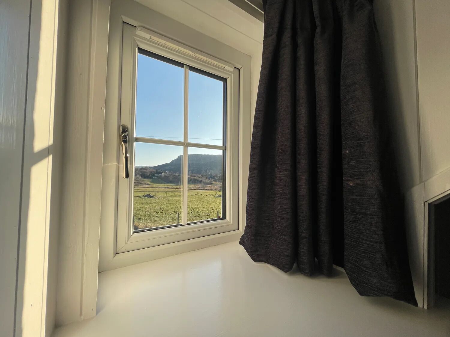 A window with a view of a green field and a hill.