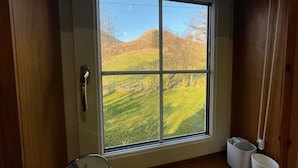 A room with a large window offering a view of a green landscape with hills and trees. - HAWTHORN DENE, pet friendly, cosy croft cottage with mountain views in Torrin (Torrin)