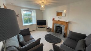 A living room with a fireplace, a television, and a large window. - HAWTHORN DENE, pet friendly, cosy croft cottage with mountain views in Torrin (Torrin)
