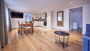 Una cocina moderna con armarios blancos, un comedor con mobiliario de madera y una pequeña mesa redonda con base de metal.