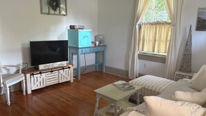 Een woonkamer met een televisie, een bijzettafeltje, een bank en een raam met gordijnen.