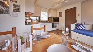 A modern kitchen with white cabinets, a dining area with a wooden table, and a small bed with a polka dot pillow.