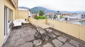 A balcony with a table and chairs, a sofa, and a view of a town and mountains in the background.