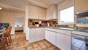 A modern kitchen with white cabinets, a large window, and a dining area with wooden chairs and a table.