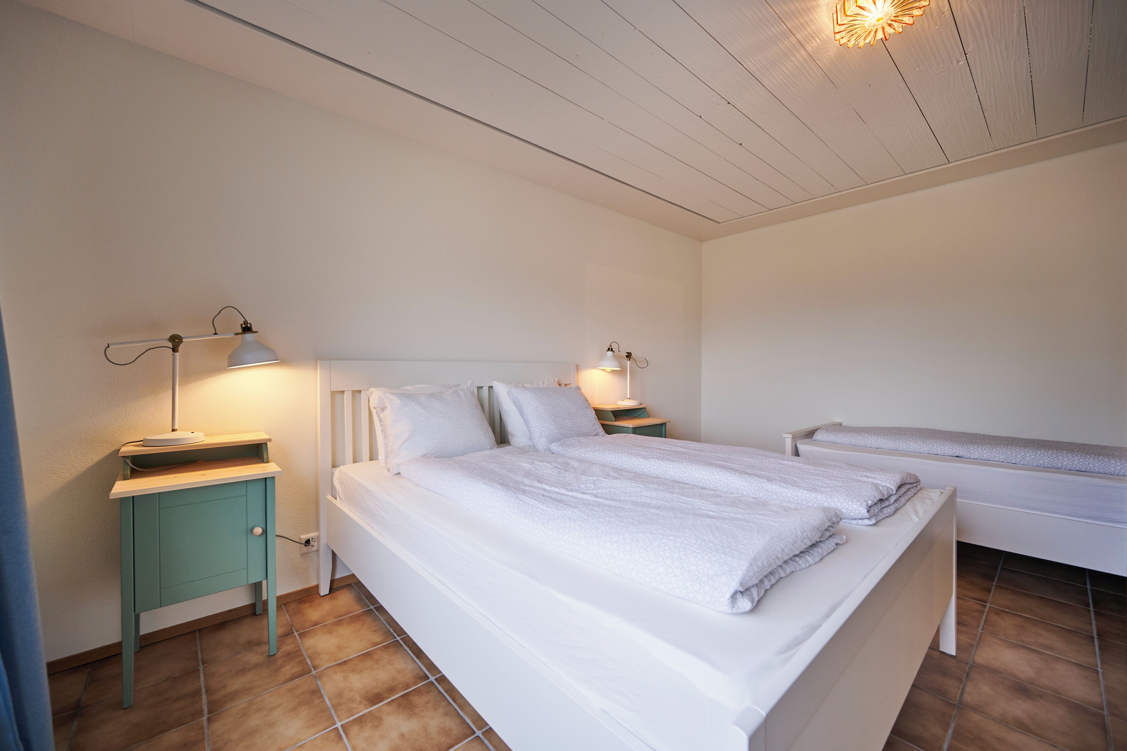 A bedroom with two beds, a nightstand with a lamp, and a wall-mounted light fixture.