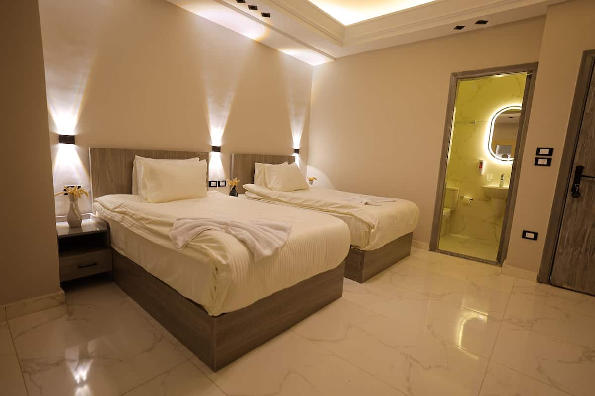 Une chambre d’hôtel avec deux lits, une table de chevet et une salle de bain visible à travers une porte ouverte.
