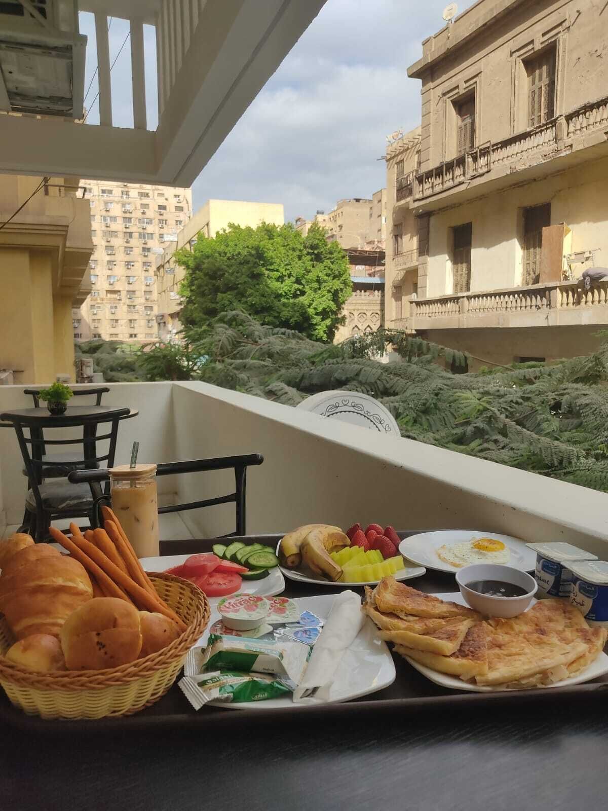 Un balcón con una mesa dispuesta para el desayuno, que incluye pan, frutas y un plato con huevos.