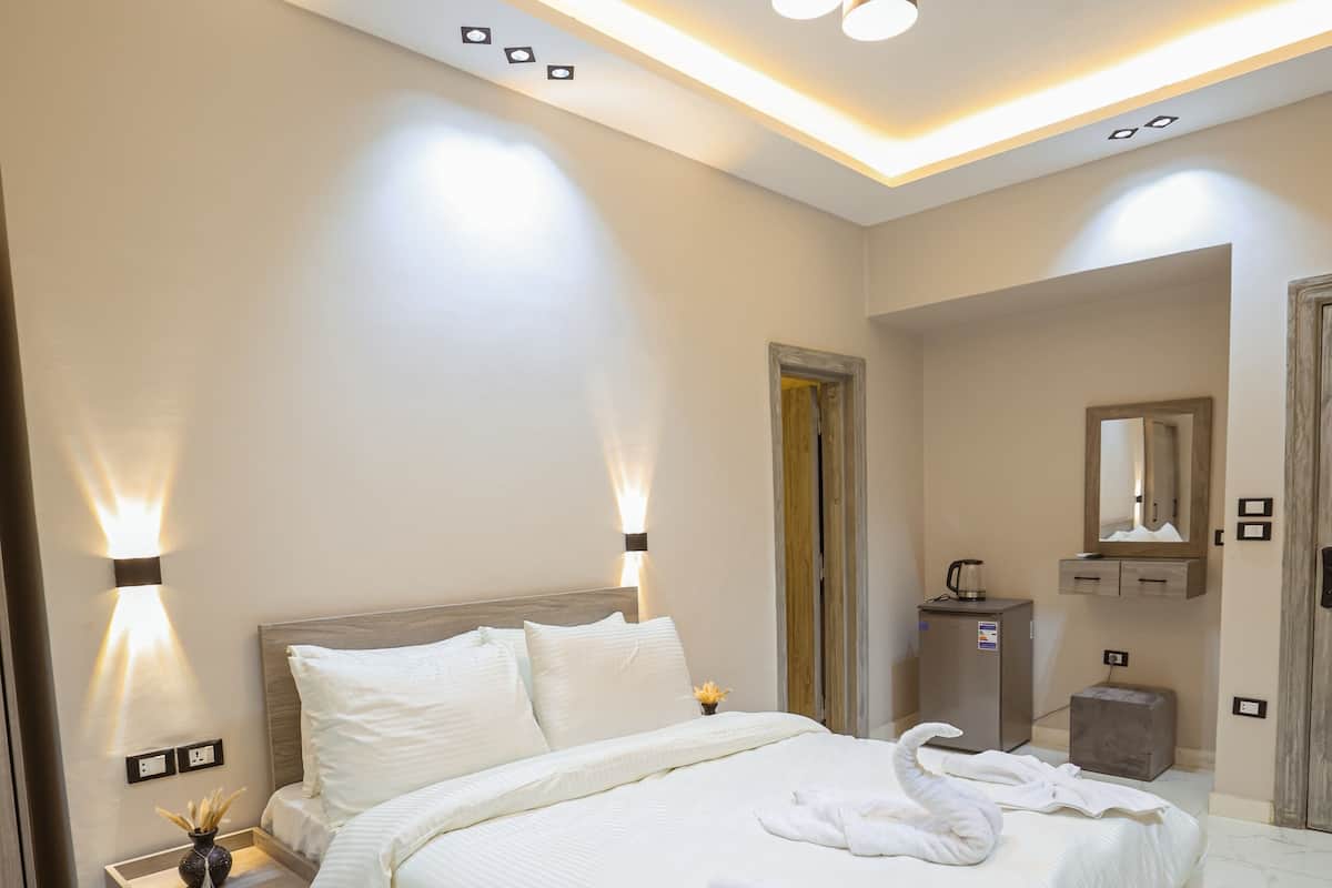 Une chambre d’hôtel moderne avec un grand lit, des tables de chevet, une coiffeuse avec un miroir et un petit bureau.