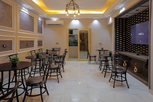A dining area with multiple tables and chairs, a modern chandelier, and a TV screen on the wall.