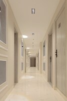 A long, narrow hallway with doors on both sides, recessed lighting, and a polished marble floor.
