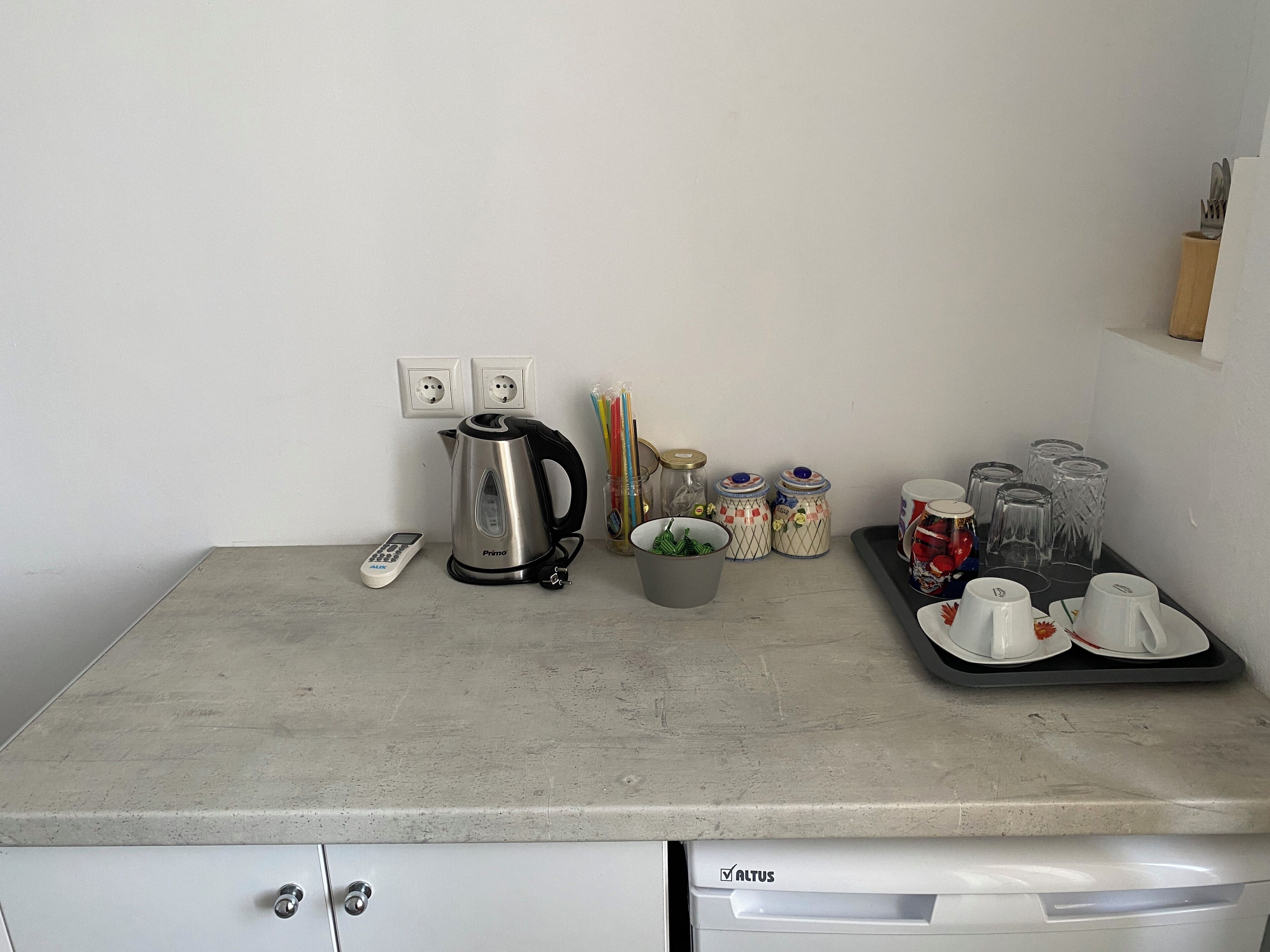 A kitchen counter with a kettle, jars, a remote, and a tray with cups and saucers.