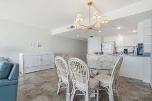 Une cuisine moderne avec des meubles blancs, un coin repas avec des chaises blanches et une table à plateau en verre.