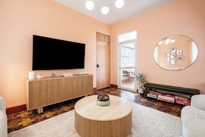 Un soggiorno con una TV a schermo piatto, un tavolino rotondo, un mobiletto in legno, uno specchio e un divano.