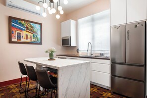 Una cocina moderna con una isla central, muebles blancos, electrodomésticos de acero inoxidable y un cuadro colorido en la pared.