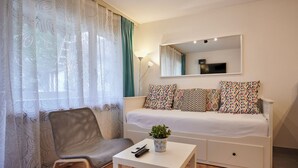 Ein Schlafzimmer mit Bett, Stuhl, kleinem Tisch, Topfpflanze und Spiegel an der Wand.