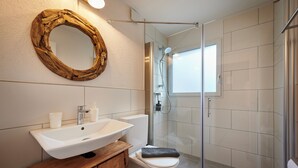 Ein modernes Badezimmer mit einem Holz-Waschtisch, einem weißen Waschbecken und einer Duschkabine aus Glas.