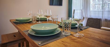 A dining table set with green plates, glasses, and cutlery, with a wooden table and a TV mounted on the wall.