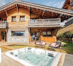 A log cabin with a hot tub, stone walls, and a balcony with chairs.