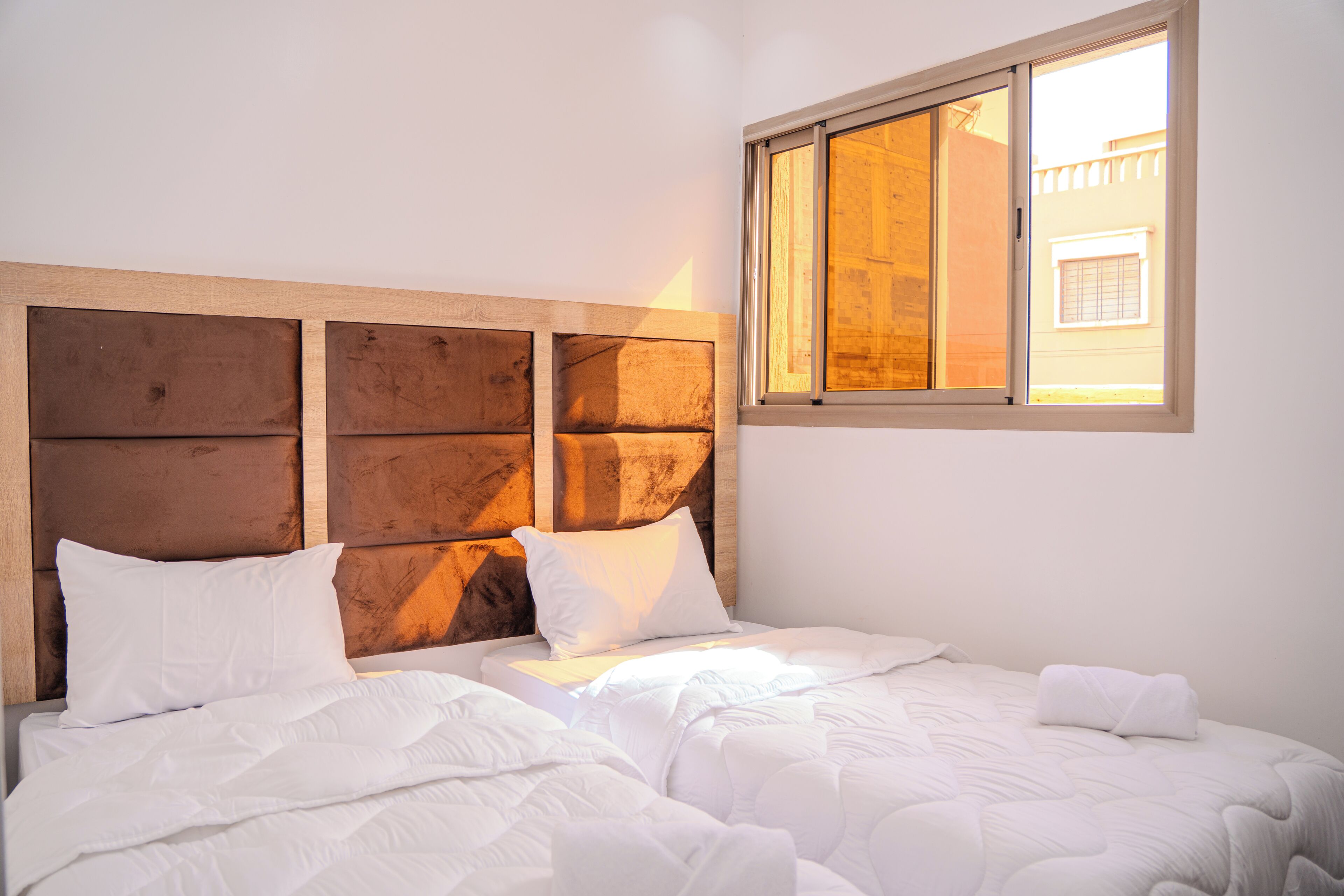 A hotel room with a wooden headboard, two beds, white bedding, and a window with a view of a building.