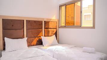 A hotel room with a wooden headboard, two beds, white bedding, and a window with a view of a building.